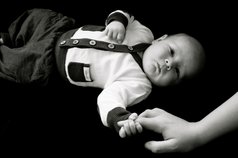Fotograf baby håller pekfinger B&W newbie kläder